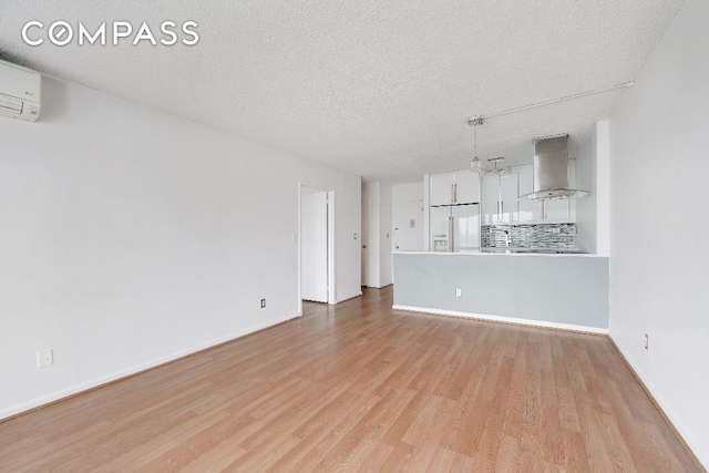 unfurnished living room featuring a textured ceiling, baseboards, a wall mounted air conditioner, and light wood-style floors