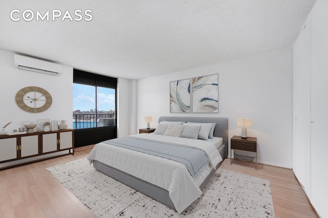 bedroom with a wall unit AC, access to exterior, light wood finished floors, and a textured ceiling