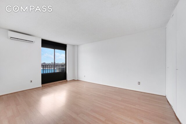 unfurnished room with a wall unit AC, light wood finished floors, and a textured ceiling