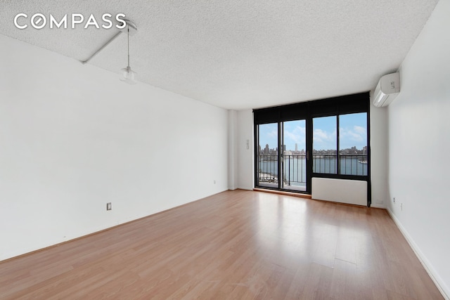 unfurnished room featuring light wood-style flooring, a wall of windows, a textured ceiling, and a wall mounted AC