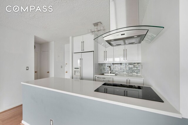 kitchen with high end fridge, island exhaust hood, a sink, white cabinets, and decorative backsplash