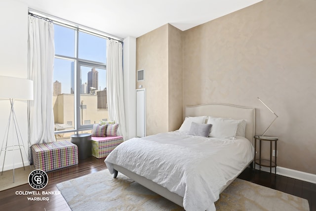 bedroom with wood finished floors, visible vents, baseboards, a view of city, and a wall of windows