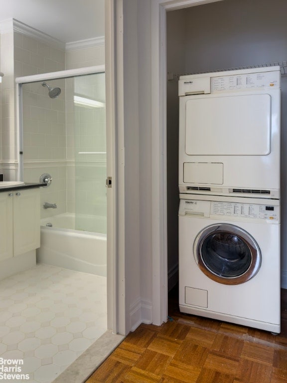 laundry area featuring ornamental molding, stacked washing maching and dryer, and dark parquet floors