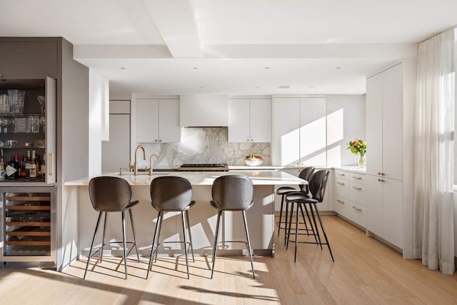 kitchen featuring a breakfast bar, white cabinets, beverage cooler, and decorative backsplash