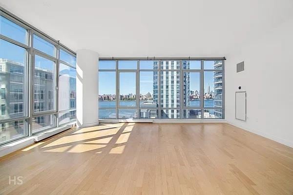 empty room featuring visible vents, a water view, wood finished floors, and floor to ceiling windows