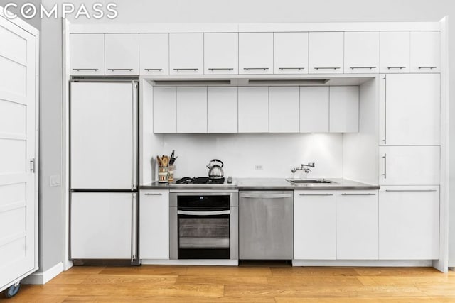 kitchen with light wood-type flooring, sink, stainless steel appliances, and white cabinetry