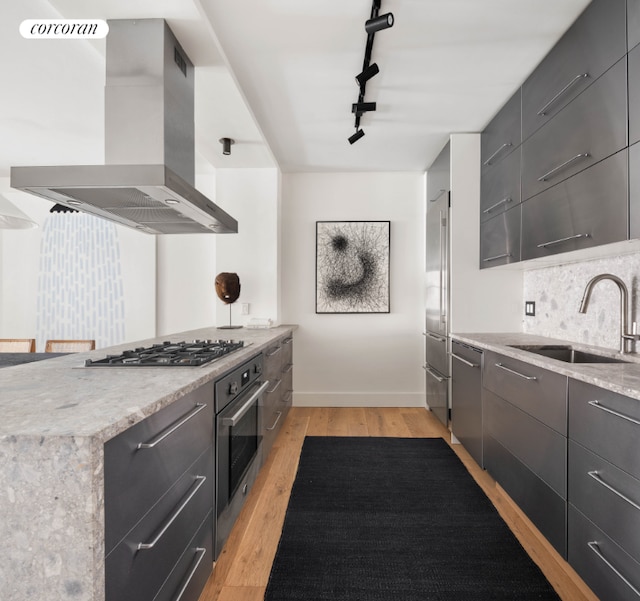 kitchen with appliances with stainless steel finishes, island range hood, tasteful backsplash, sink, and light hardwood / wood-style floors