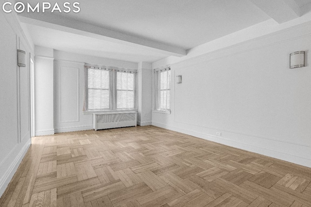 unfurnished room with light parquet flooring, beamed ceiling, and radiator heating unit