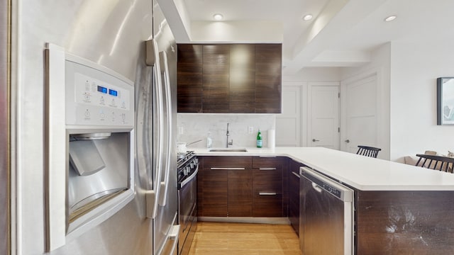 kitchen with dark brown cabinetry, sink, light hardwood / wood-style flooring, appliances with stainless steel finishes, and kitchen peninsula