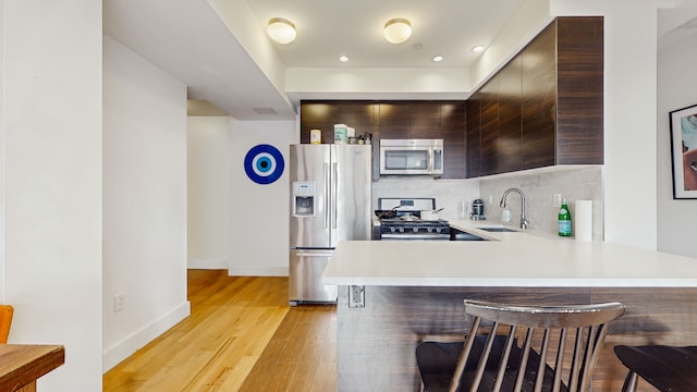 kitchen with appliances with stainless steel finishes, a sink, modern cabinets, a kitchen bar, and light countertops