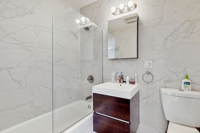 full bathroom featuring tiled shower / bath, vanity, toilet, and tile walls