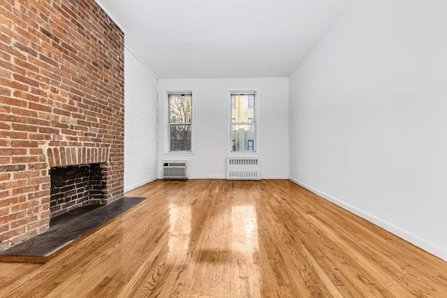 unfurnished living room with light wood-type flooring, radiator, a wall mounted AC, and a fireplace