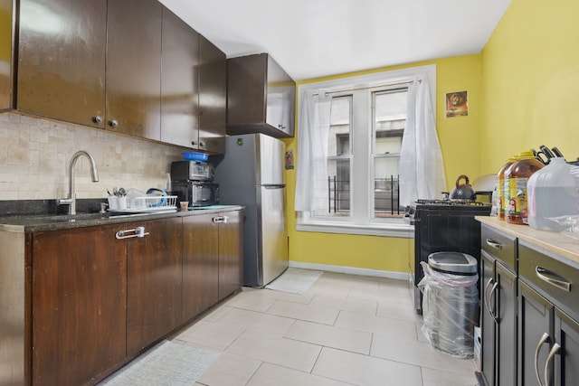 kitchen with gas stove, tasteful backsplash, stainless steel refrigerator, dark brown cabinetry, and sink