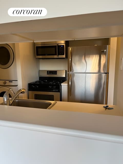 kitchen with a sink, stainless steel appliances, light countertops, and stacked washing maching and dryer