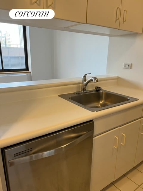 kitchen with a sink, dishwasher, light tile patterned flooring, and light countertops