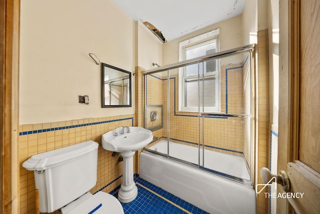 bathroom with tile patterned flooring, tile walls, shower / bath combination with glass door, and toilet