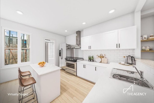 kitchen with white cabinets, appliances with stainless steel finishes, wall chimney exhaust hood, sink, and backsplash