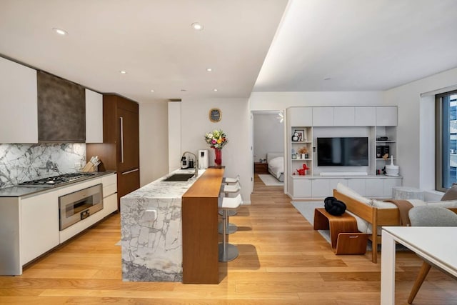 kitchen with stainless steel gas stovetop, decorative backsplash, sink, white cabinetry, and wall oven