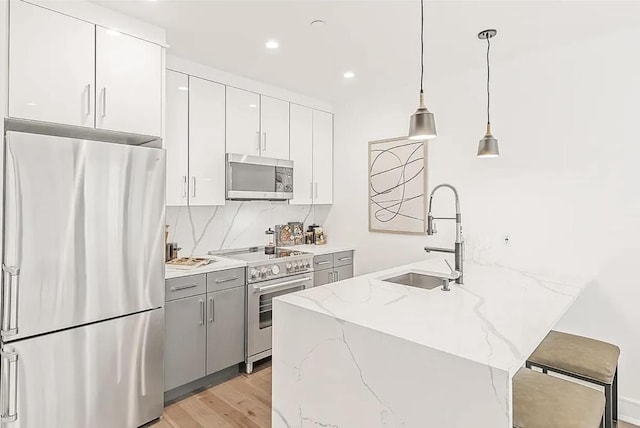 kitchen featuring hanging light fixtures, appliances with stainless steel finishes, white cabinetry, a sink, and light stone countertops