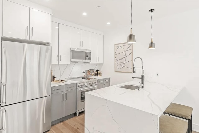 kitchen featuring white cabinets, hanging light fixtures, a sink, light wood-style flooring, and appliances with stainless steel finishes