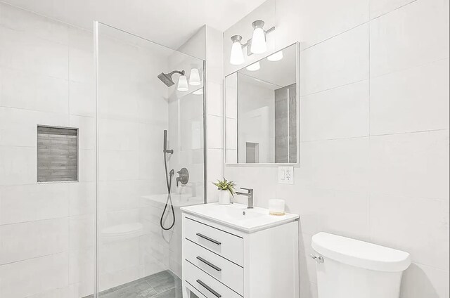 bathroom featuring vanity, toilet, tile walls, and a tile shower