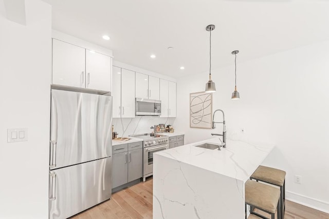 kitchen featuring decorative light fixtures, a center island with sink, stainless steel appliances, white cabinets, and a sink