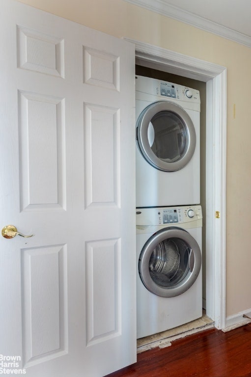 washroom with dark wood-type flooring, crown molding, and stacked washing maching and dryer