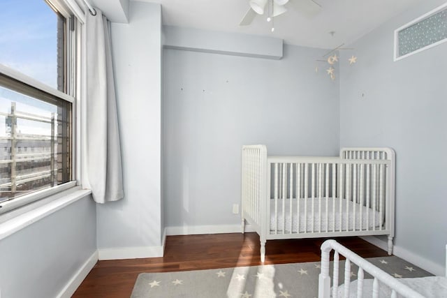 bedroom with ceiling fan, wood-type flooring, and a crib