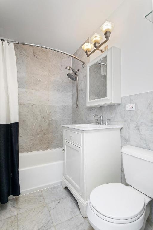 full bathroom featuring toilet, vanity, tile walls, and shower / bath combo with shower curtain