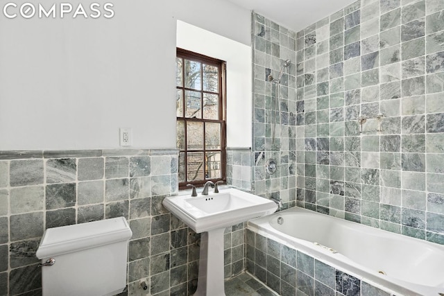 bathroom with toilet, tiled shower / bath combo, and tile walls