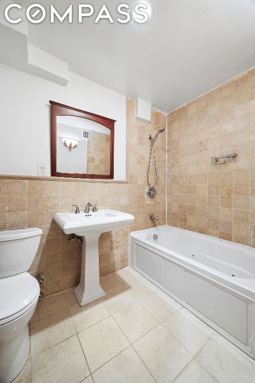 full bathroom with toilet, tiled shower / bath combo, tile walls, and sink