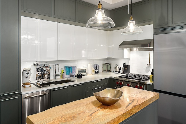 kitchen featuring a sink, decorative backsplash, stainless steel appliances, under cabinet range hood, and wood counters