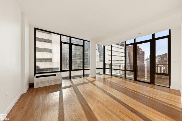 spare room featuring heating unit, wood-type flooring, and floor to ceiling windows