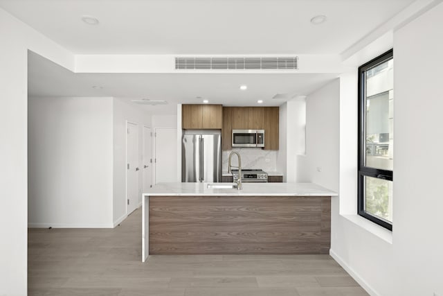 kitchen with tasteful backsplash, stainless steel appliances, kitchen peninsula, and light wood-type flooring