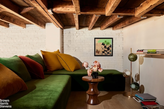 living area with brick wall, wood finished floors, and beam ceiling