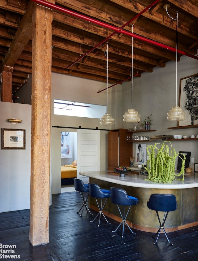 bar featuring pendant lighting, a towering ceiling, a barn door, dark wood-type flooring, and beamed ceiling