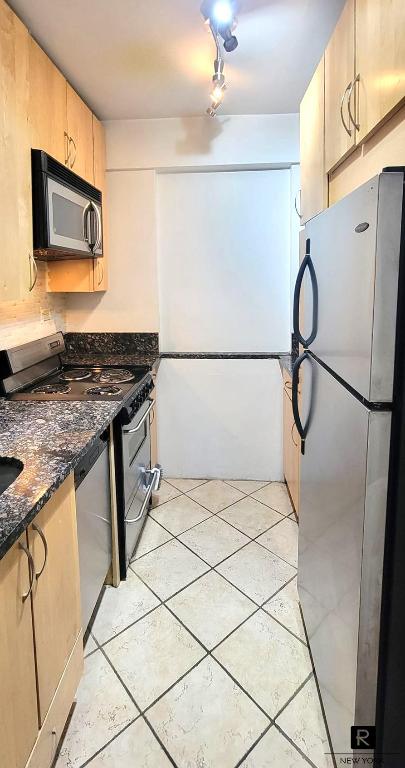 kitchen with stainless steel appliances, light brown cabinetry, light tile patterned floors, and dark stone counters