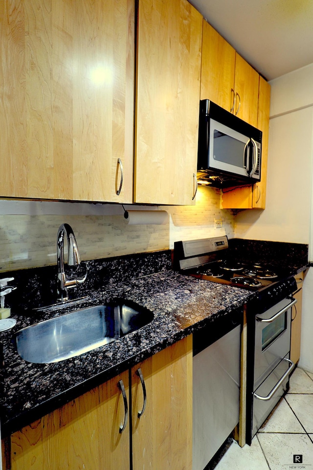 kitchen with dark stone counters, stainless steel appliances, light tile patterned flooring, and a sink