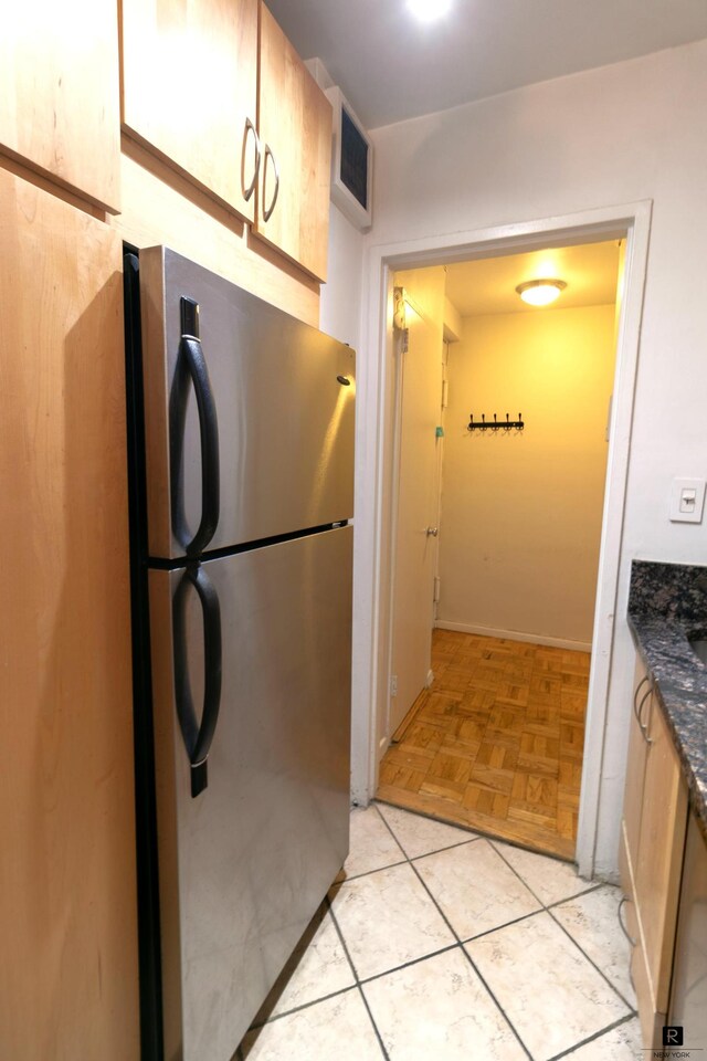 kitchen with light parquet floors, dark stone countertops, stainless steel fridge, and light brown cabinetry