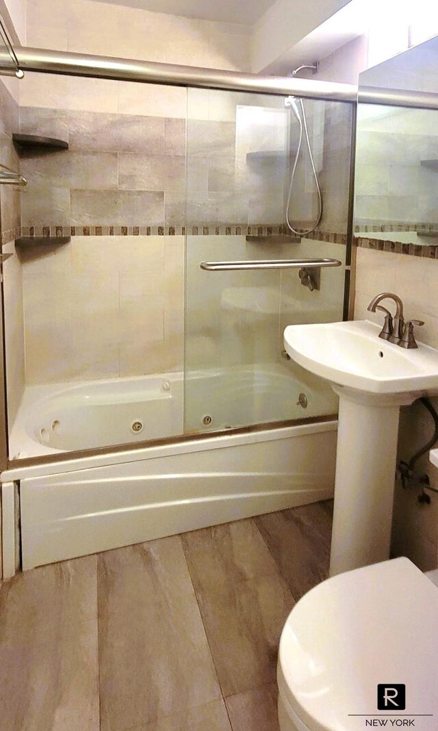 bathroom featuring toilet, bath / shower combo with glass door, hardwood / wood-style floors, and tile walls