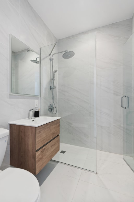 bathroom with vanity, toilet, a shower with door, and tile walls