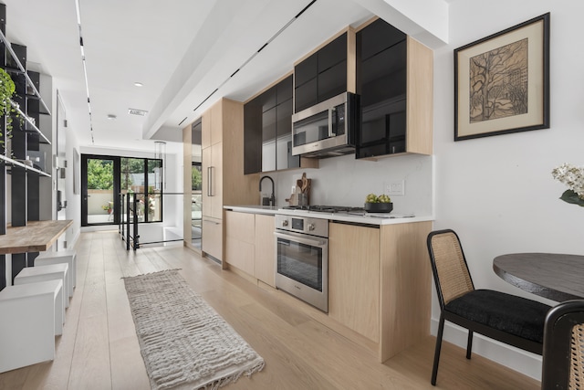 kitchen featuring light wood finished floors, stainless steel appliances, light countertops, decorative backsplash, and modern cabinets