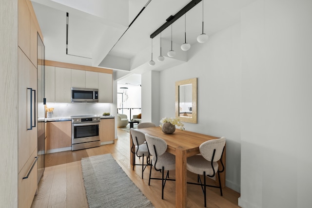 kitchen featuring pendant lighting, appliances with stainless steel finishes, white cabinetry, a towering ceiling, and light wood-type flooring