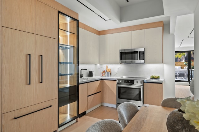 kitchen featuring light brown cabinetry, sink, backsplash, light hardwood / wood-style floors, and stainless steel appliances