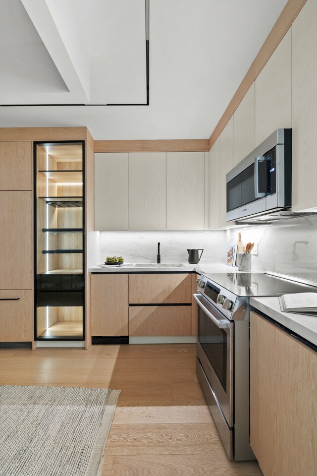 kitchen with sink, stainless steel appliances, tasteful backsplash, light wood-type flooring, and light brown cabinets