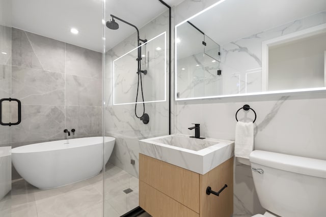 bathroom with toilet, vanity, tile walls, a freestanding bath, and a marble finish shower