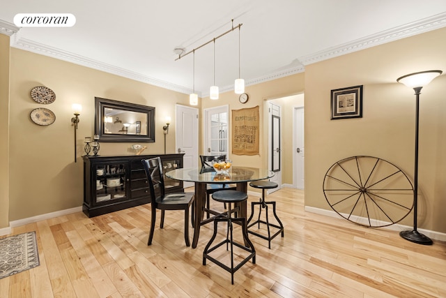 dining space featuring rail lighting, ornamental molding, and light hardwood / wood-style flooring