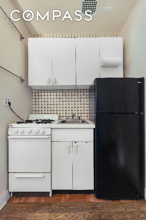 kitchen with dark hardwood / wood-style floors, black fridge, sink, white range with gas stovetop, and white cabinets