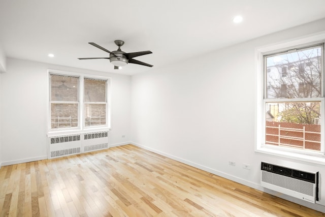 spare room with a wall unit AC, radiator heating unit, a ceiling fan, wood finished floors, and baseboards