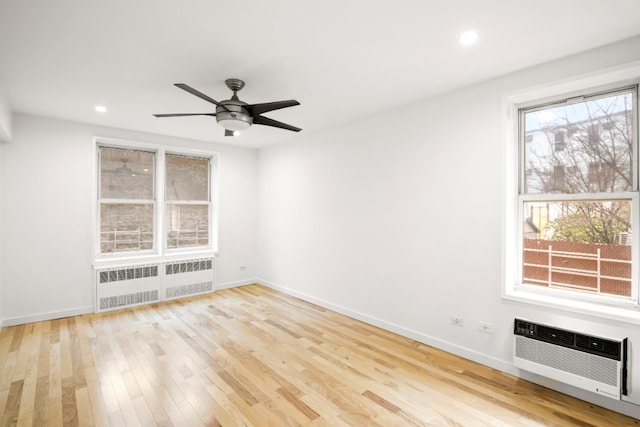 empty room with ceiling fan, radiator heating unit, a wall mounted air conditioner, and light wood-type flooring